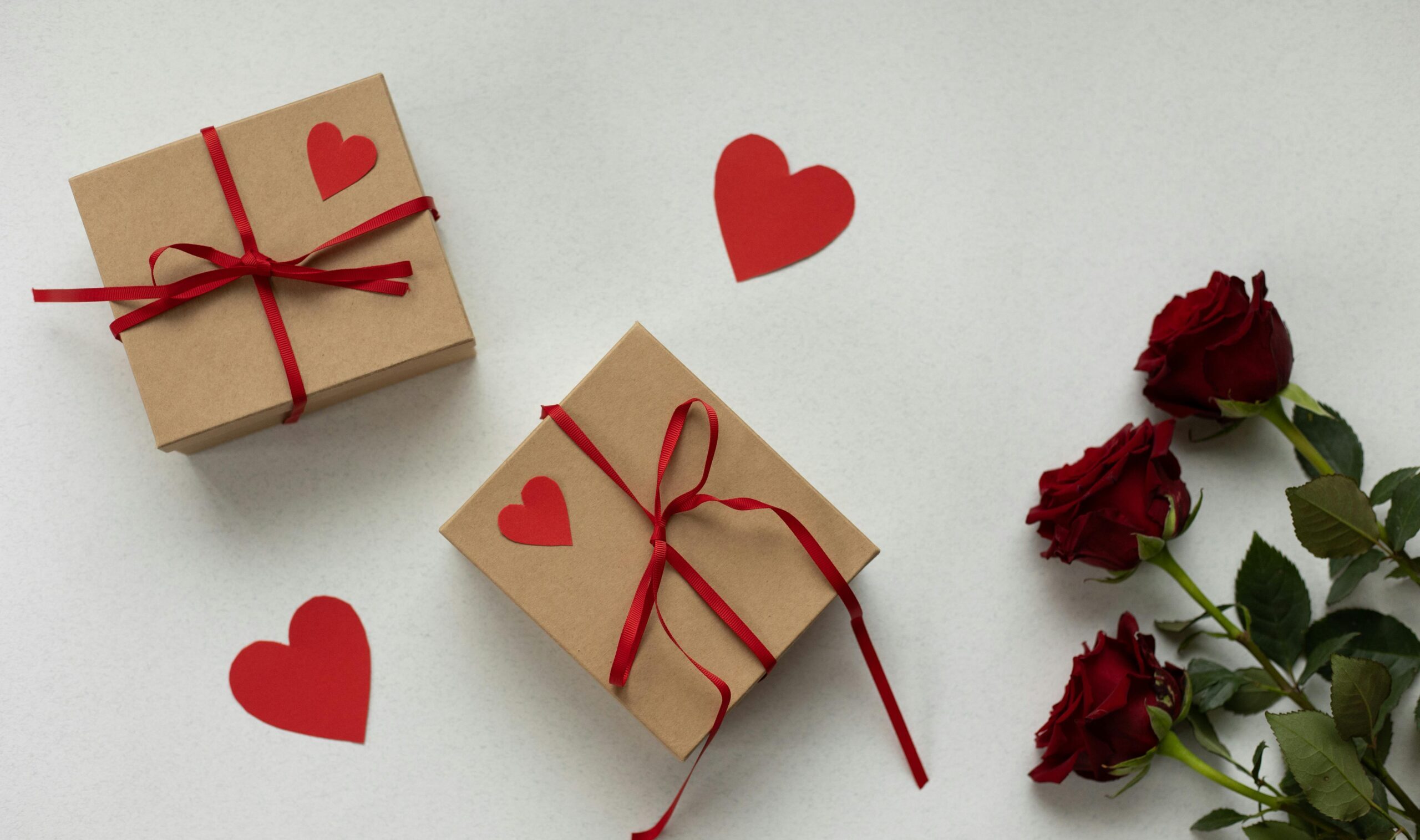 Flat lay of wrapped gifts, red roses, and heart shapes for a romantic Valentine's celebration.